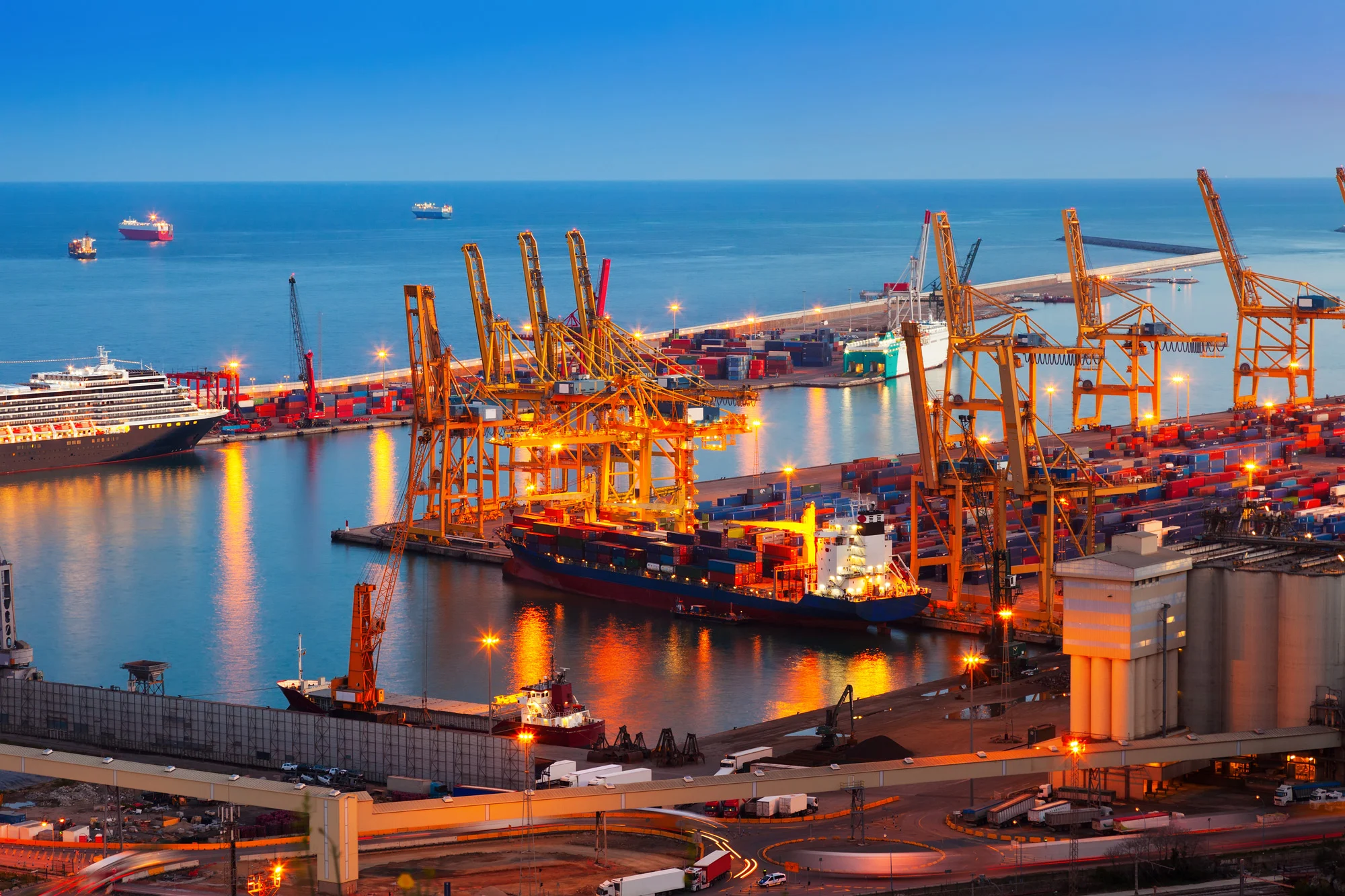Illuminated seaport cargo terminal with container gantry cranes and cargo ships operating under Disrupt-X HSEQ standards